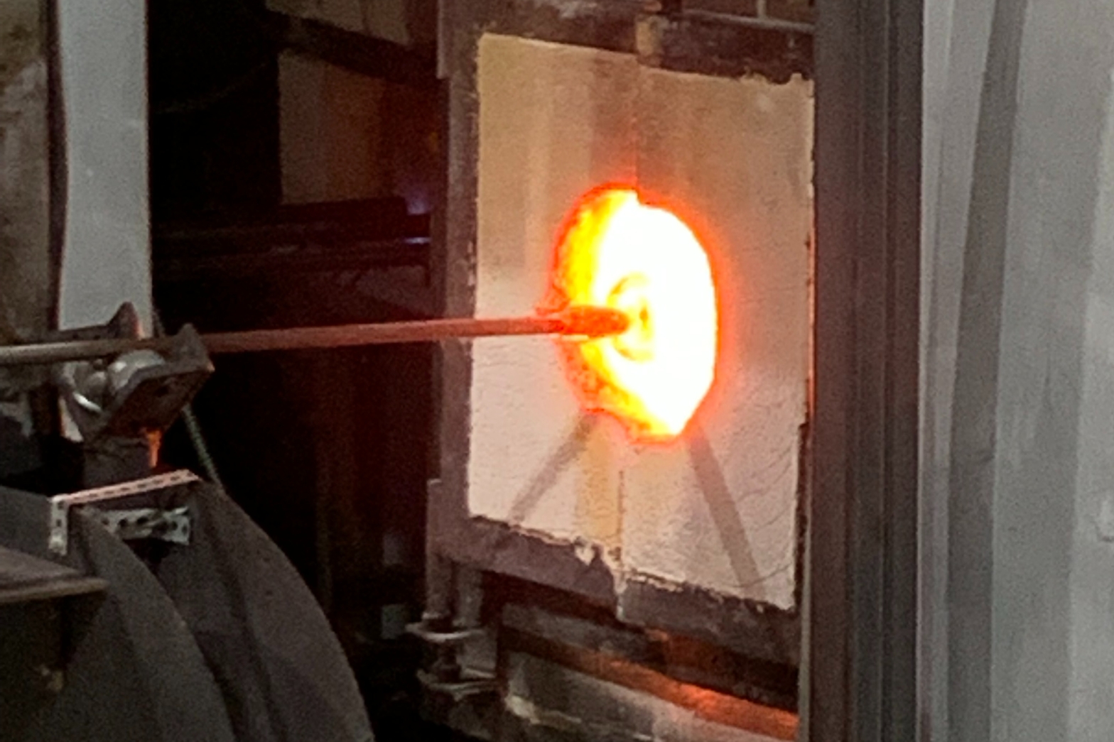 a glass furnace with a glowing circular hole. There's a pipe going into it with a blob of glass attached