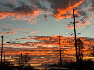 the sky in the morning, with thin clouds it in yellow, orange, and red. There are telephone lines on the right, and a car at the bottom